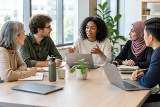 Petite équipe diverse échangeant autour d’une table lors d’un rituel de communication en entreprise.